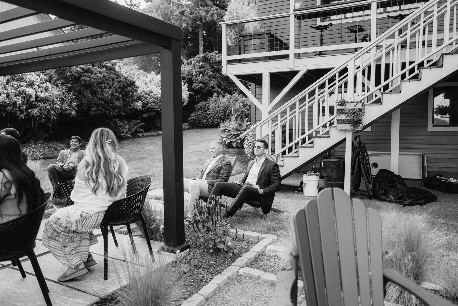 Black and white photo of wedding guests relaxing in Adirondack chairs at an outdoor reception.