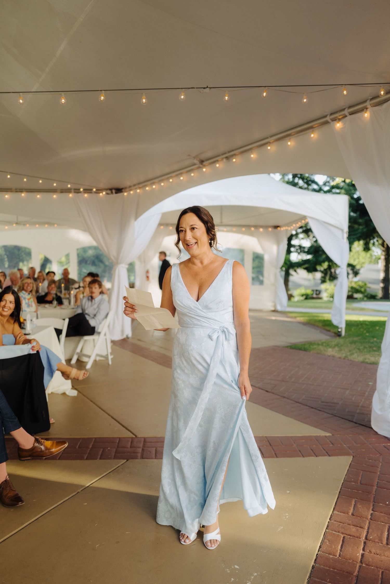Wedding celebration under white tent with string lights and brick paved floor.