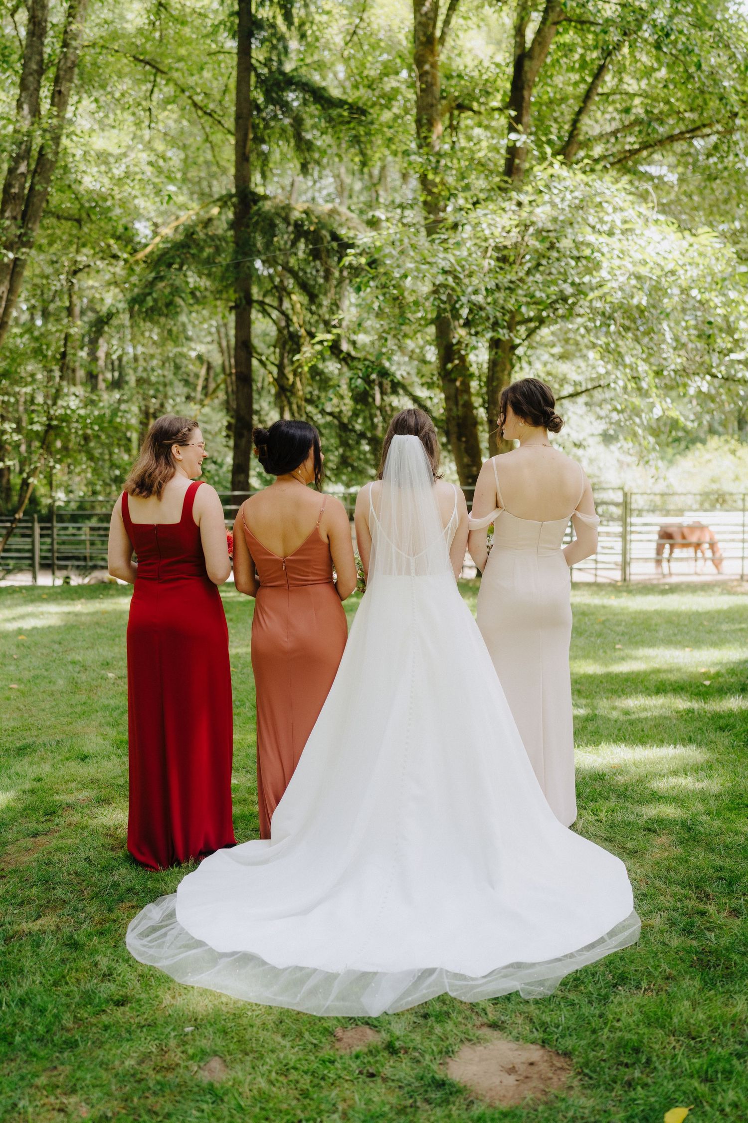 A bridal party in autumn-toned dresses stands together on a lush green lawn during an outdoor wedding.