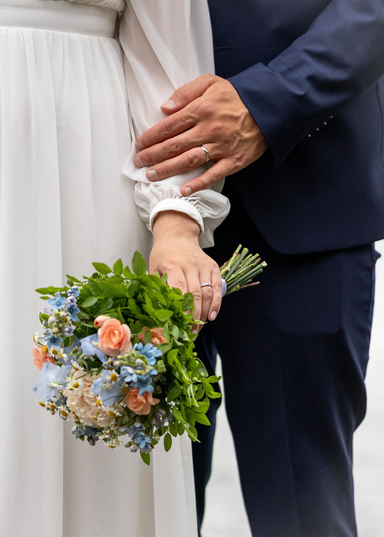 Lähikuva hääparista, jossa sulhanen pitää kättään morsiamen ranteella ja morsiamella on kädessään värikäs hääkimppu. Hääkuvaus Uusimaa.