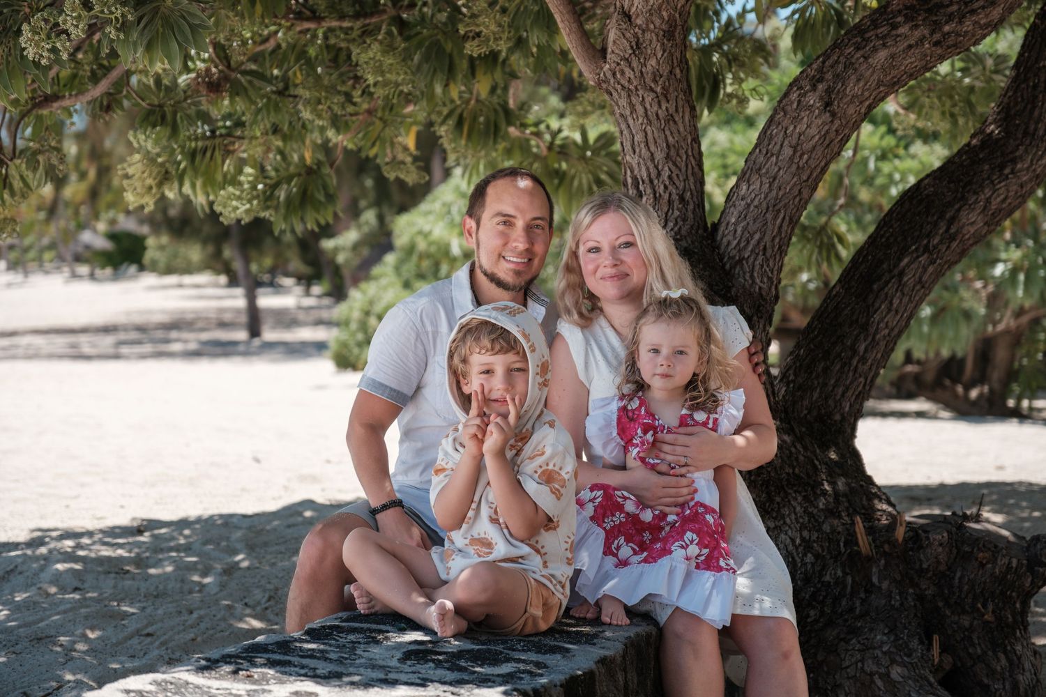 Family group poses casually under shady tree on sunny day.