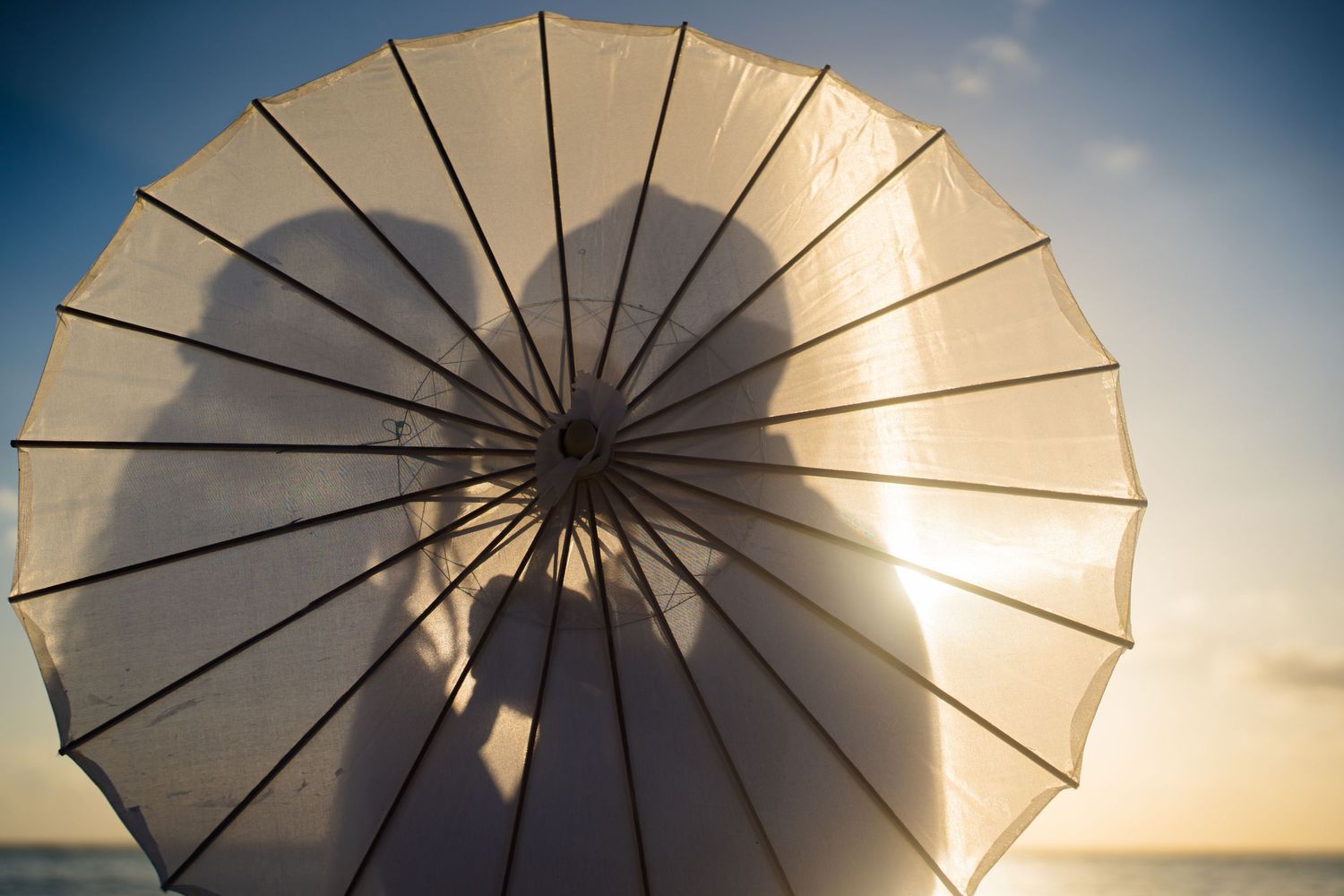 Silhouette of couple behind white parasol umbrella at sunset on beach.