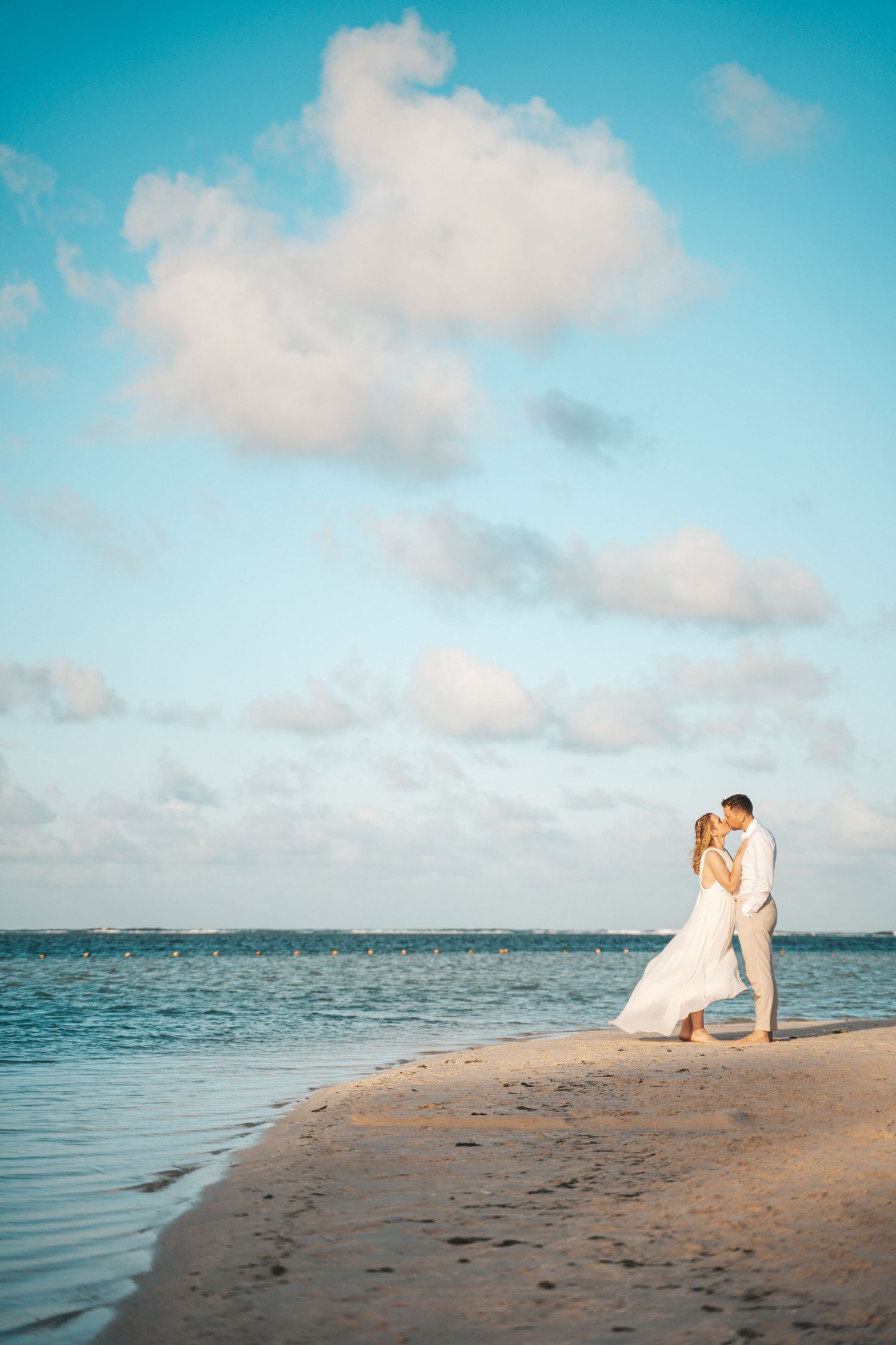 Turquoise ocean view with couple on sandy beach during sunset photo session.