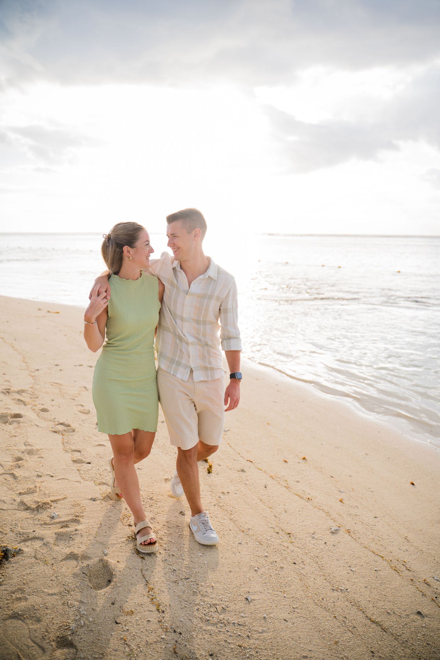 Couple in casual summer outfits walking together on sandy beach at sunset.