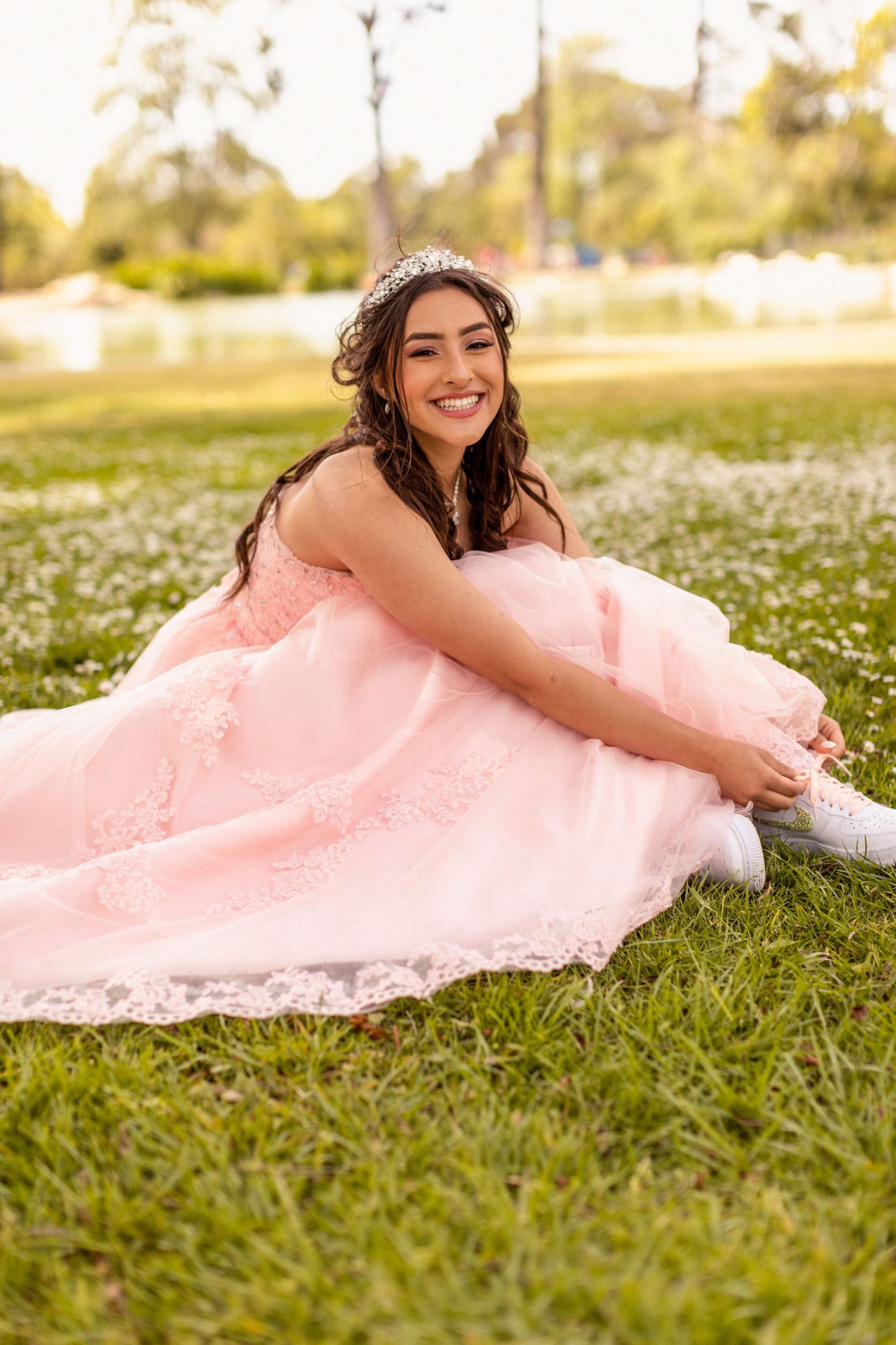 Pink quinceañera dress sparkles in sunlit field of white flowers.