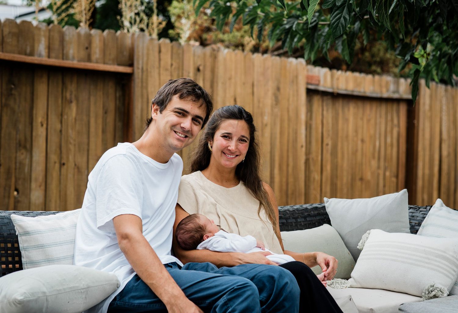 Relaxed outdoor photography session on white cushions against wooden fence backdrop.