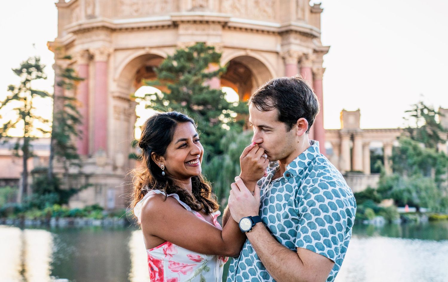 Two people laughing together in front of an ornate pink building during golden hour.