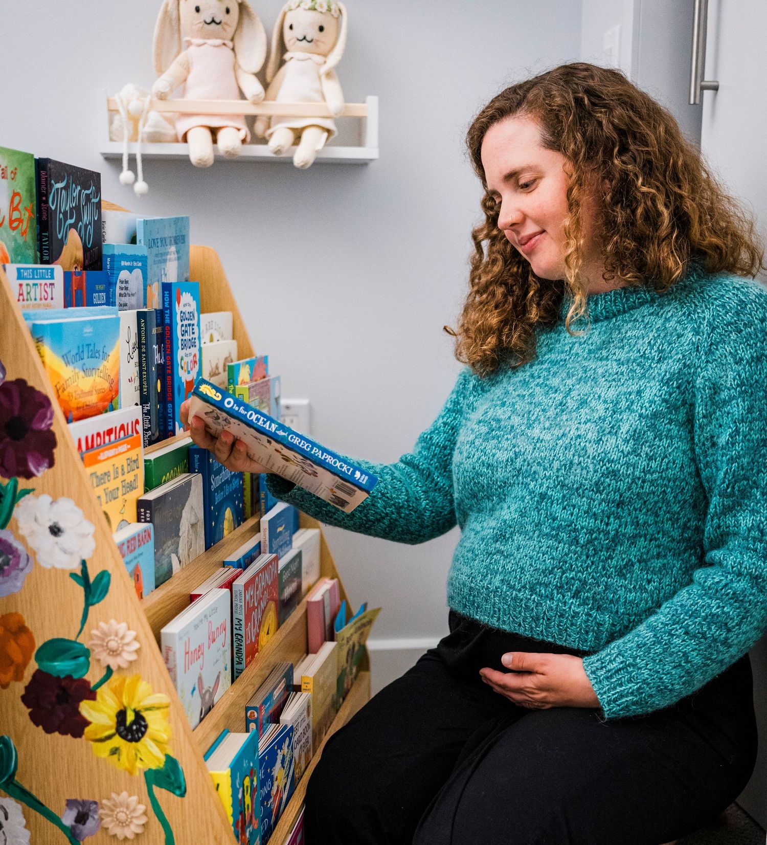A person wearing a blue sweater browsing children's books on stylish nursery shelves.