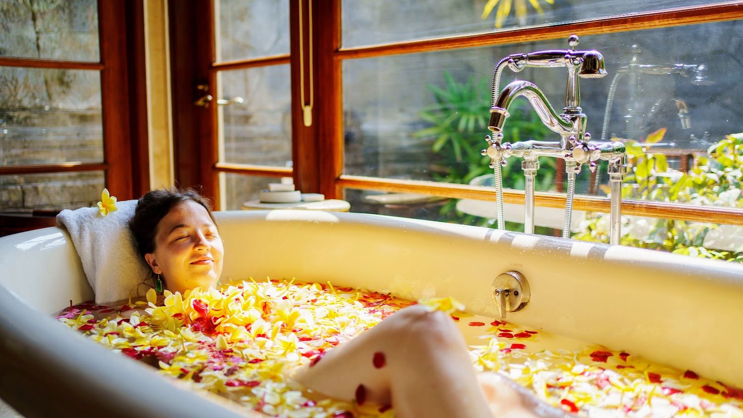 Decorative bathtub filled with floating flower petals and natural light streaming through windows.