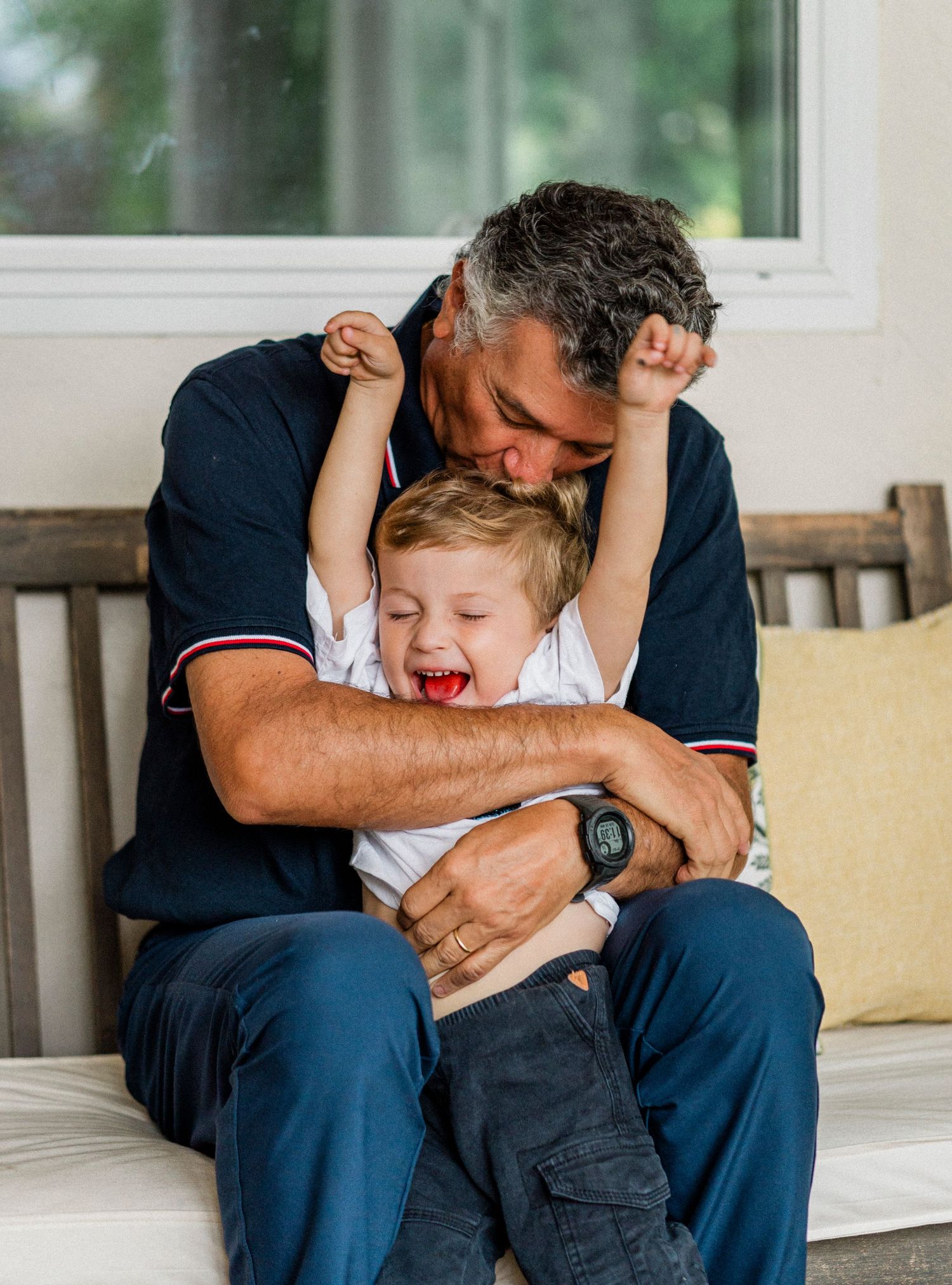 A heartwarming candid moment shows playful interaction and laughter between parent and child on a porch bench.