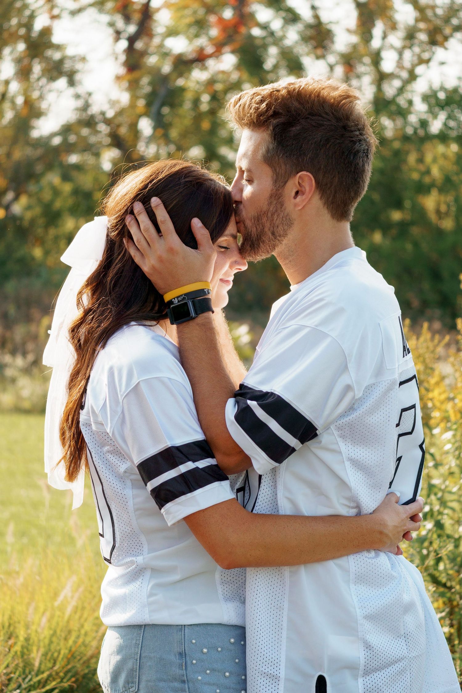 Tender embrace between couple wearing matching sports jerseys in sunlit field.