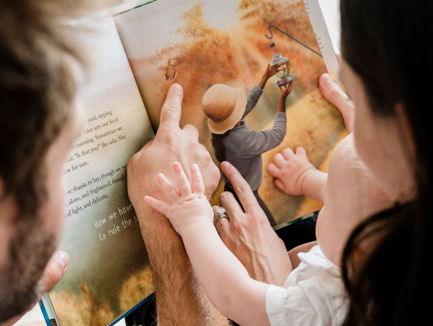 Family reading story time together while pointing at illustrations in a book.
