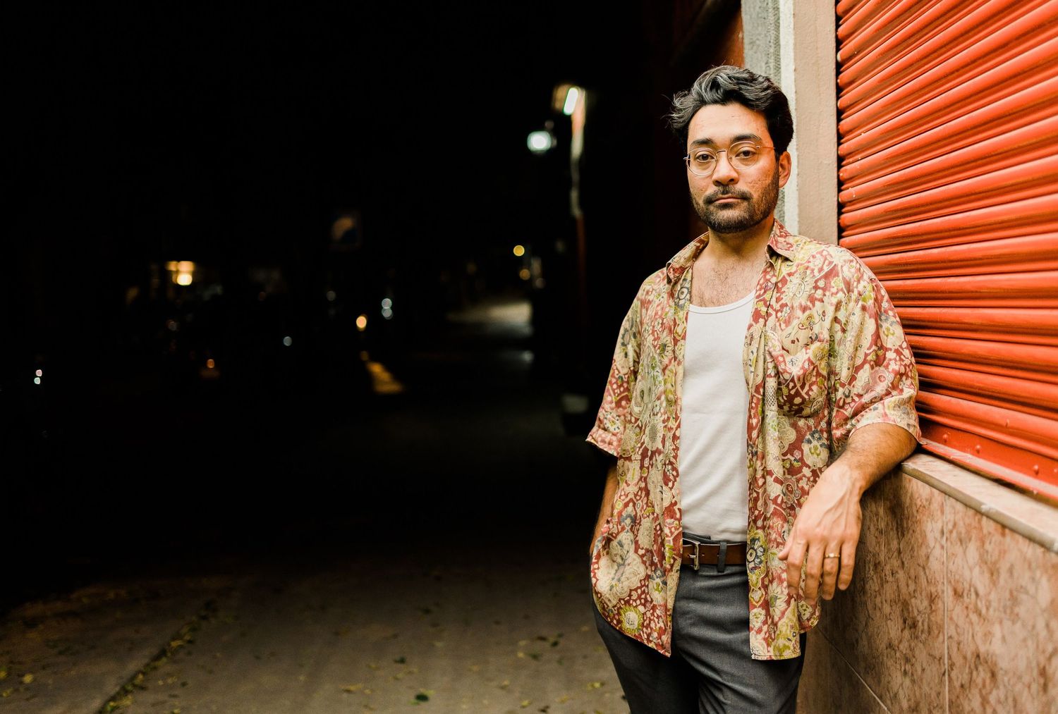 Person wearing floral shirt stands against orange storage unit wall at dusk.
