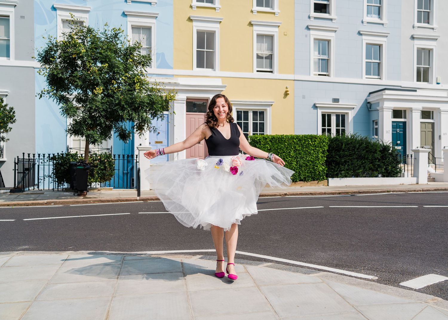 Colorful row of pastel-painted townhouses with uniform windows along a quiet street and a woman dancing.