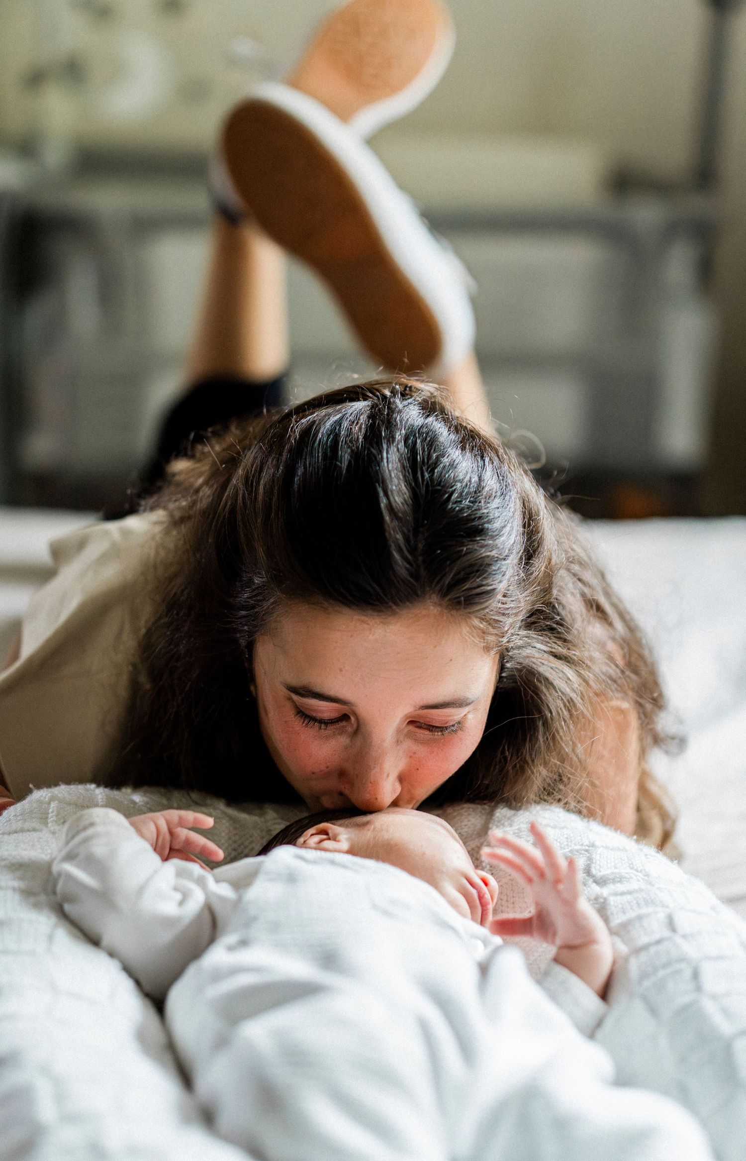 Close-up shots capture tender kisses and cuddles with a baby wrapped in white blankets.