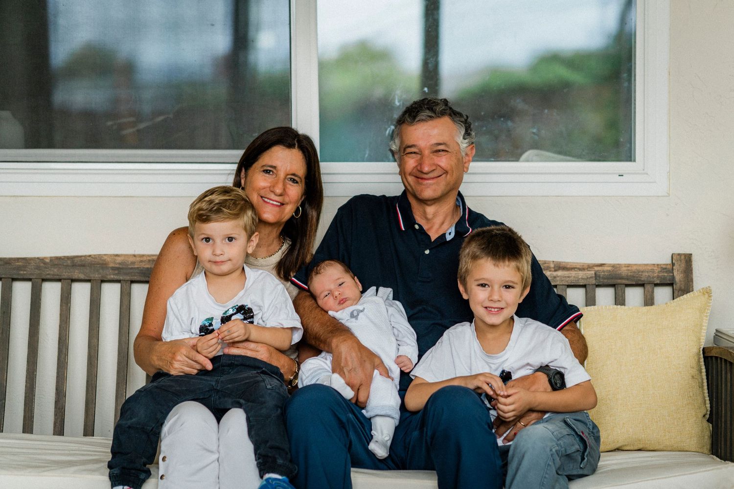 Family members gather on a porch bench for a casual outdoor portrait.