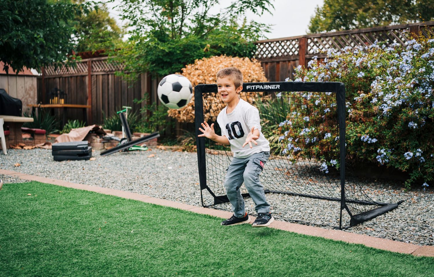 A sequence of images showing a soccer ball being kicked in a backyard with stone landscaping and wooden fencing.
