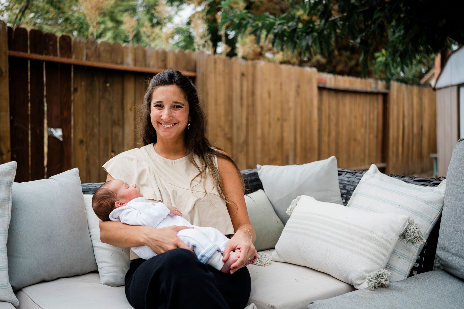 Family members share tender moments with a newborn baby while relaxing on a couch outdoors.