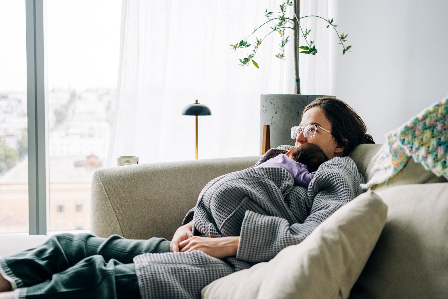 Candid moments of family relaxation on a gray couch near large windows with natural light.