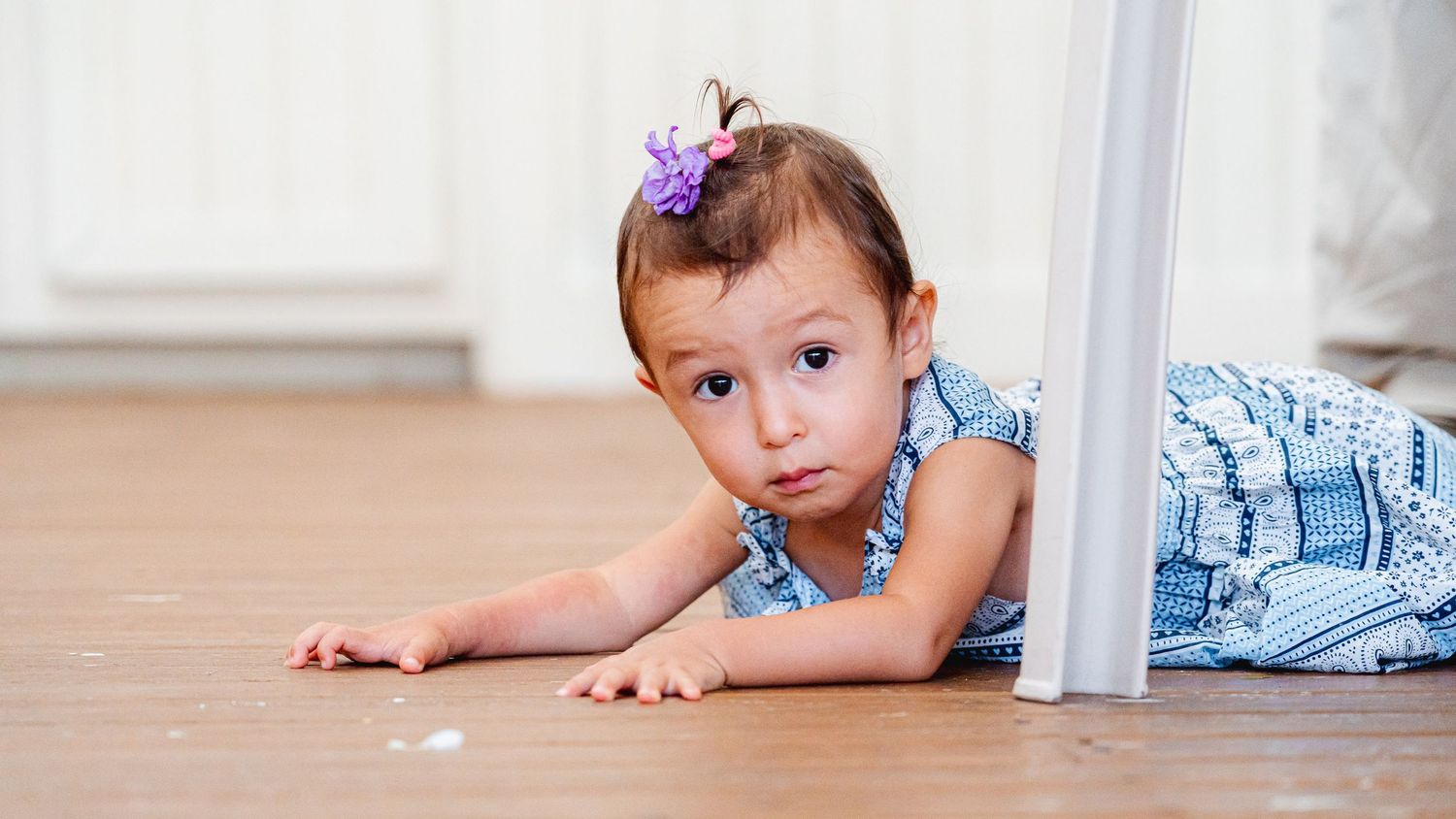 A child crawling on a wooden floor during a family gathering.