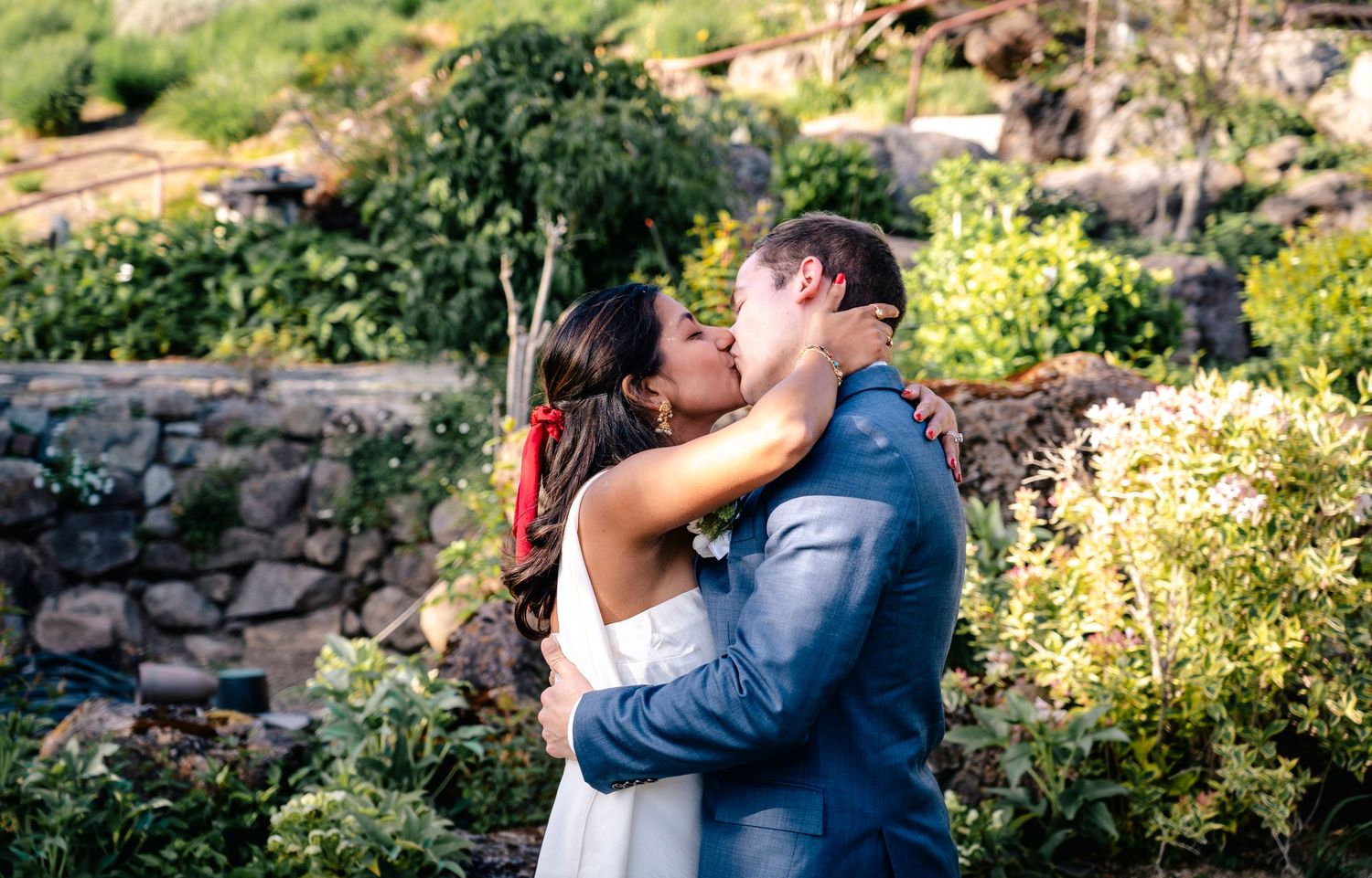Couple shares a romantic moment in a lush garden setting surrounded by green foliage on their wedding day.