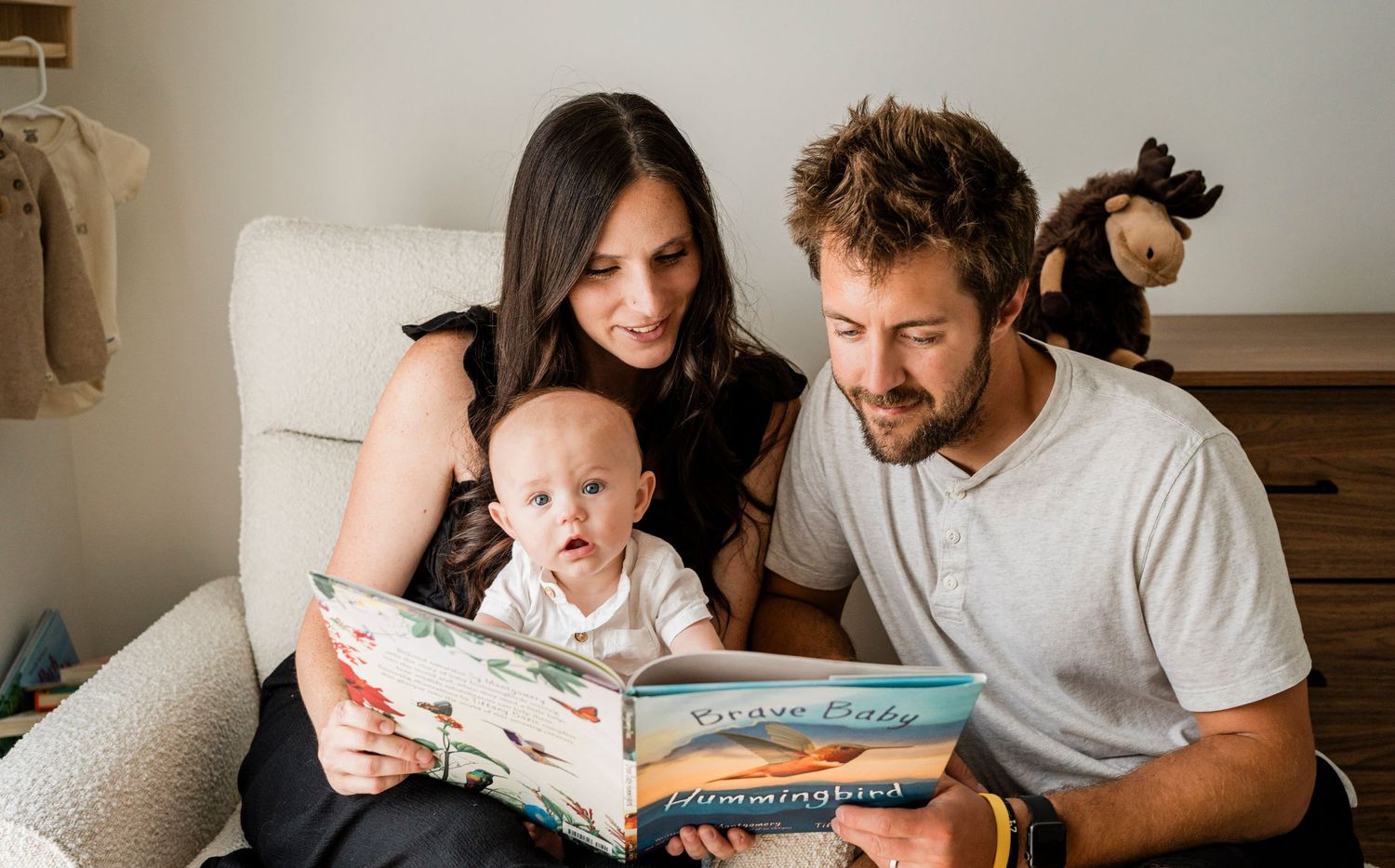 Family sharing storytime together on comfortable nursery chair at home.