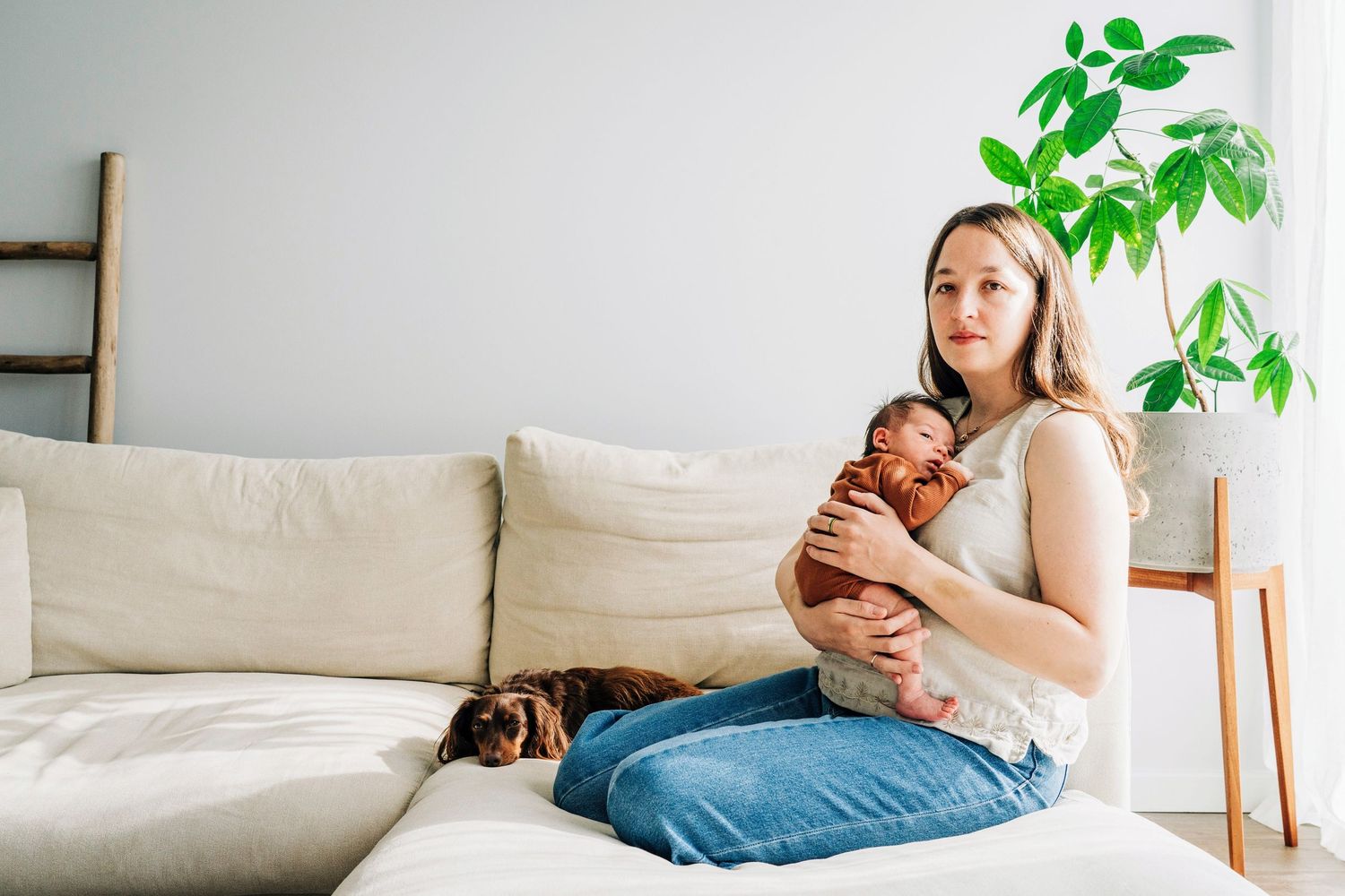 A tender moment with a newborn baby on a cream colored sofa with a green plant nearby.