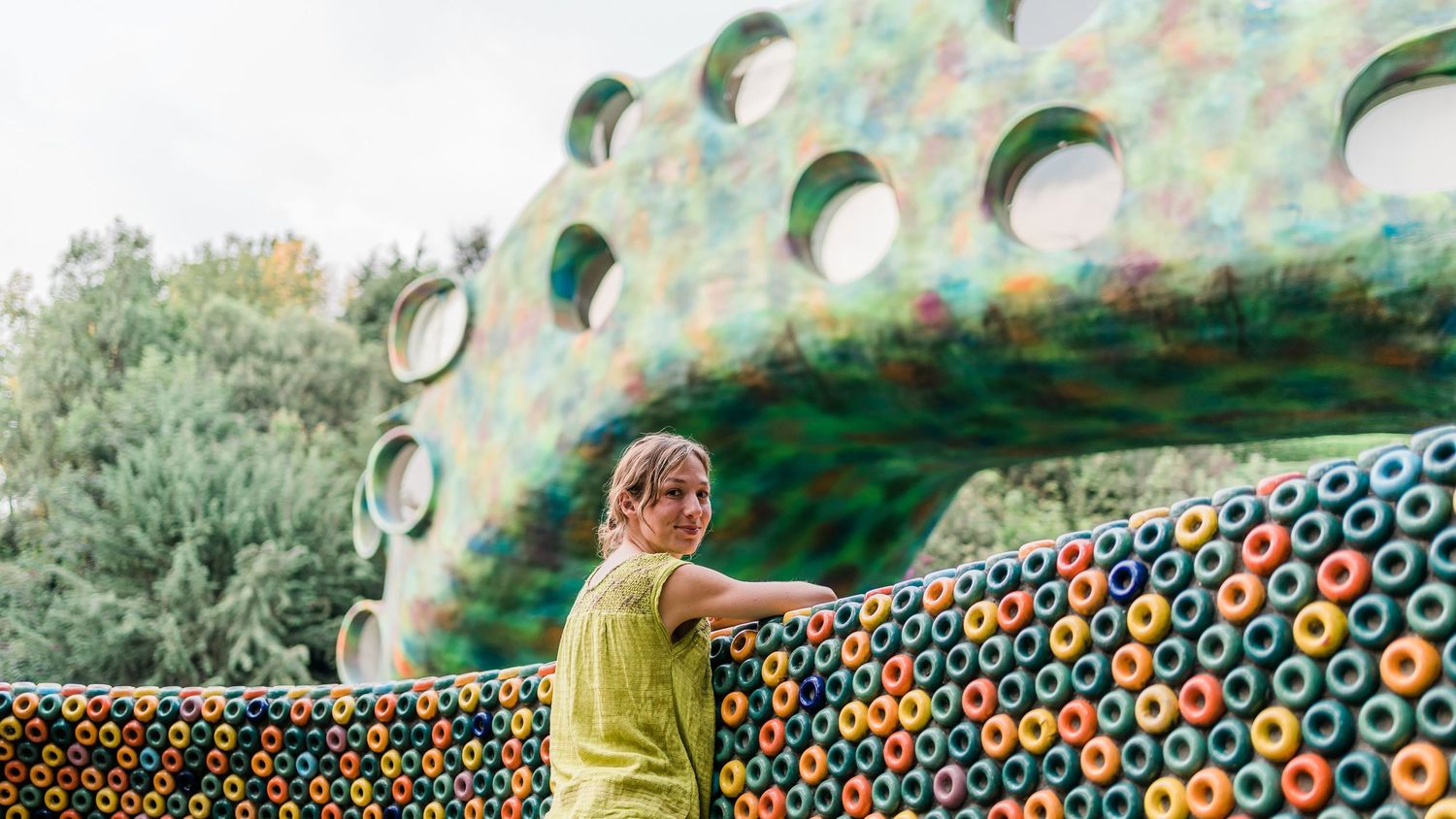 Figure in yellow clothing stands near a colorful mosaic wall with circular patterns.
