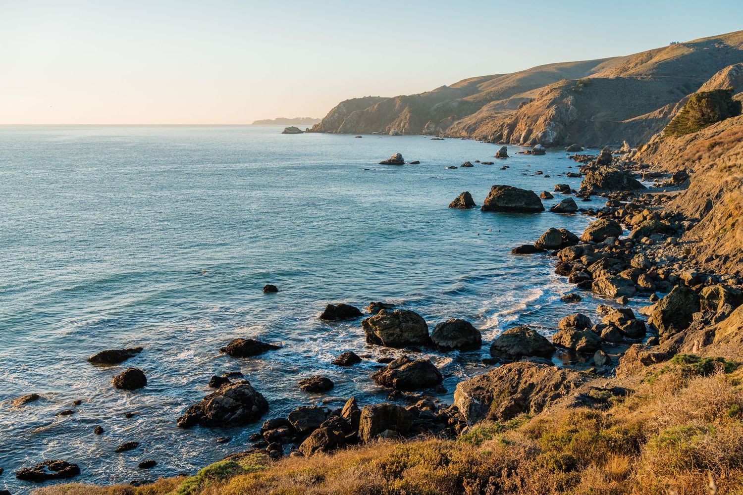 Dramatic rocky coastline with rugged cliffs and blue ocean waters along Big Sur, California during golden hour.