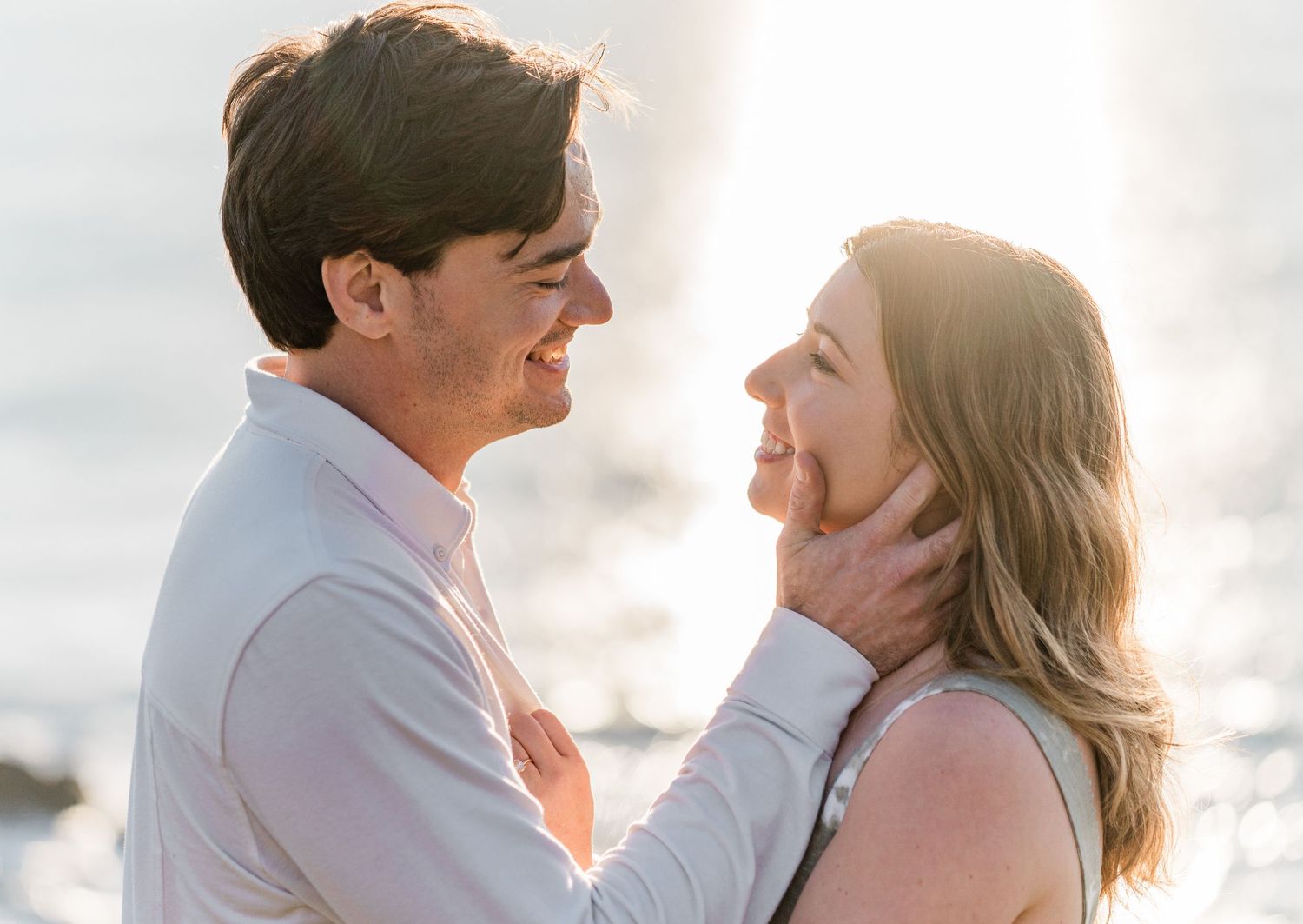 A romantic couple embraces during a sunset photoshoot on the beach with soft glowing light in the background.