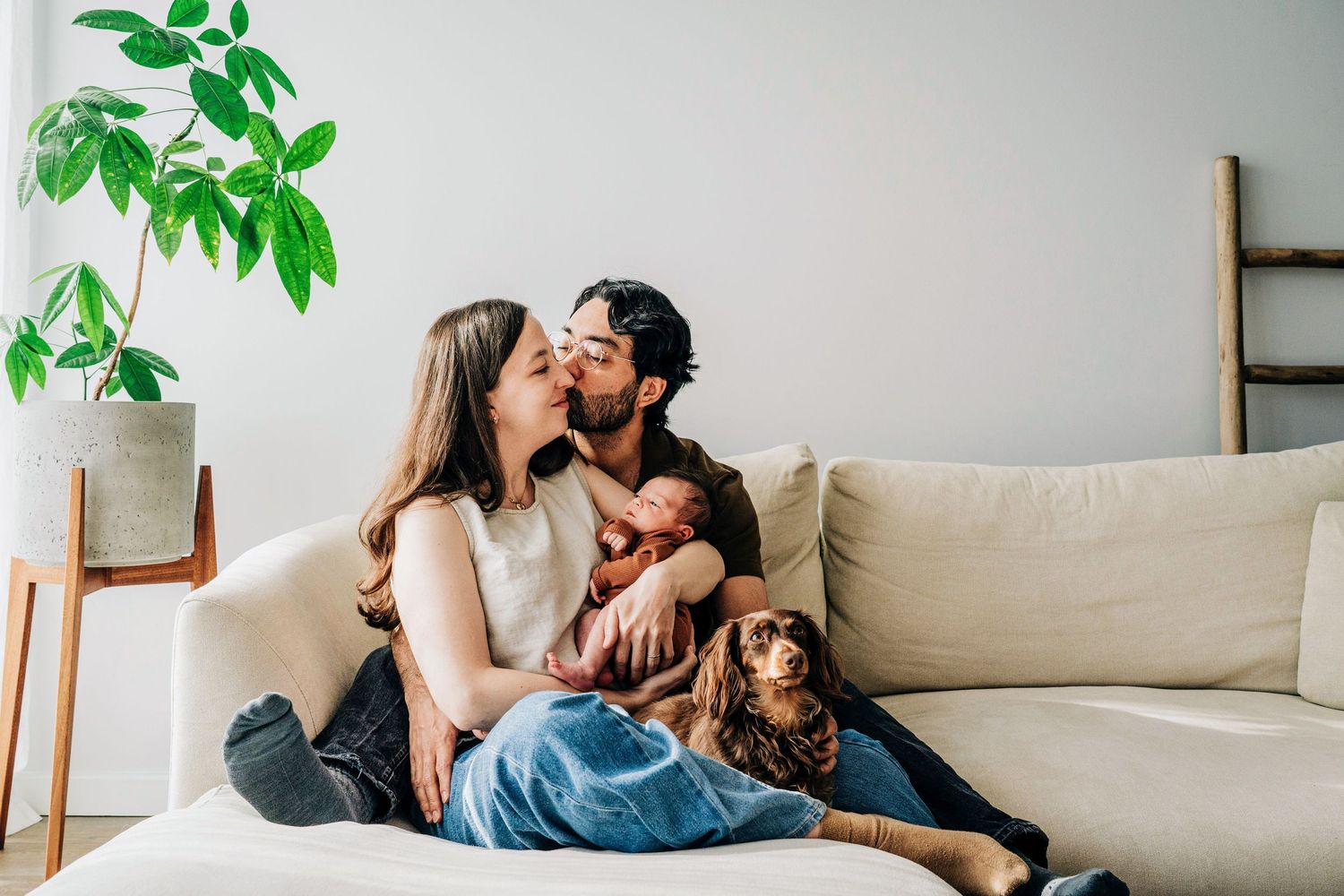 Intimate indoor scene of couple with their newborn baby and dog in modern minimalist well-decorated home.
