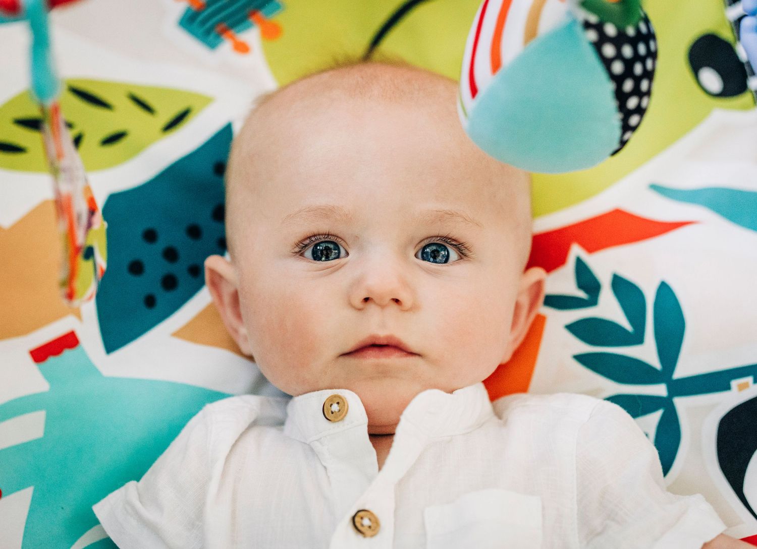 Baby wearing white outfit against colorful abstract floral play mat with turquoise and orange patterns.
