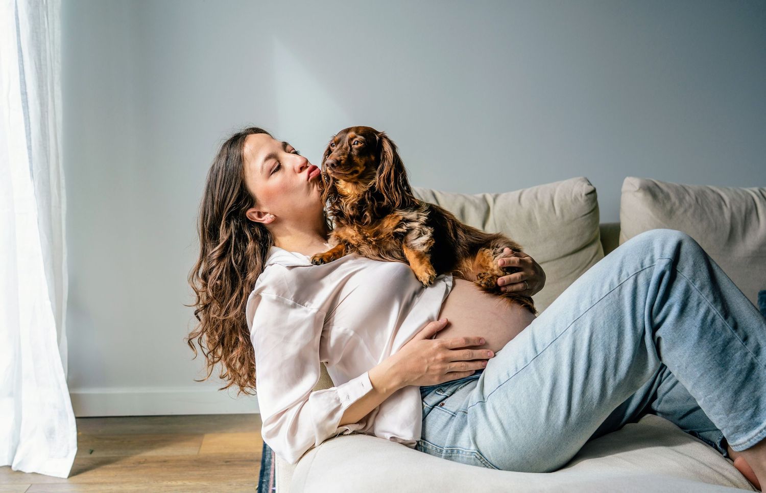 An intimate photoshoot of a cozy cuddle session on a white couch with natural window lighting.