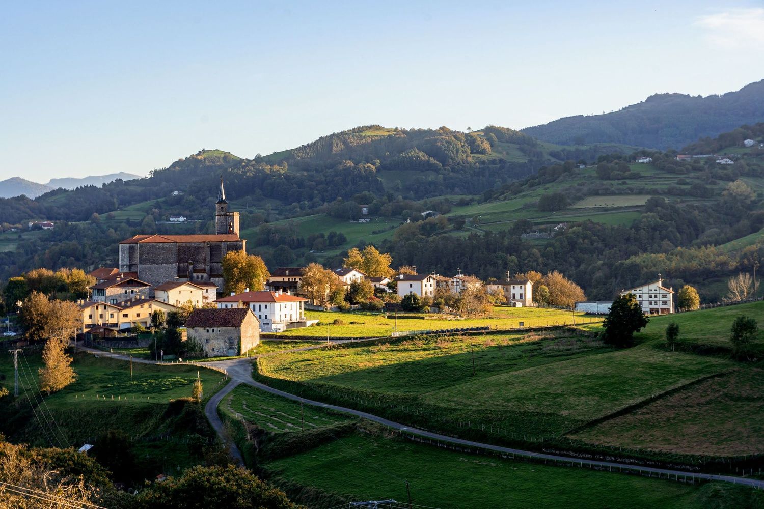 Rolling green hills and mountains in rural countryside with scattered buildings in golden sunlight.