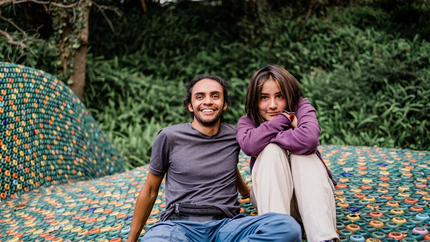 Two people relax together on a colorful mosaic bench in a garden setting.