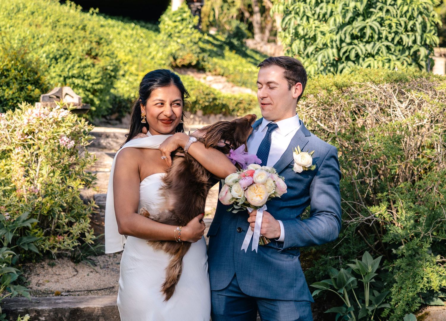 Wedding party celebrates together in a sunlit garden setting with joyful expressions.
