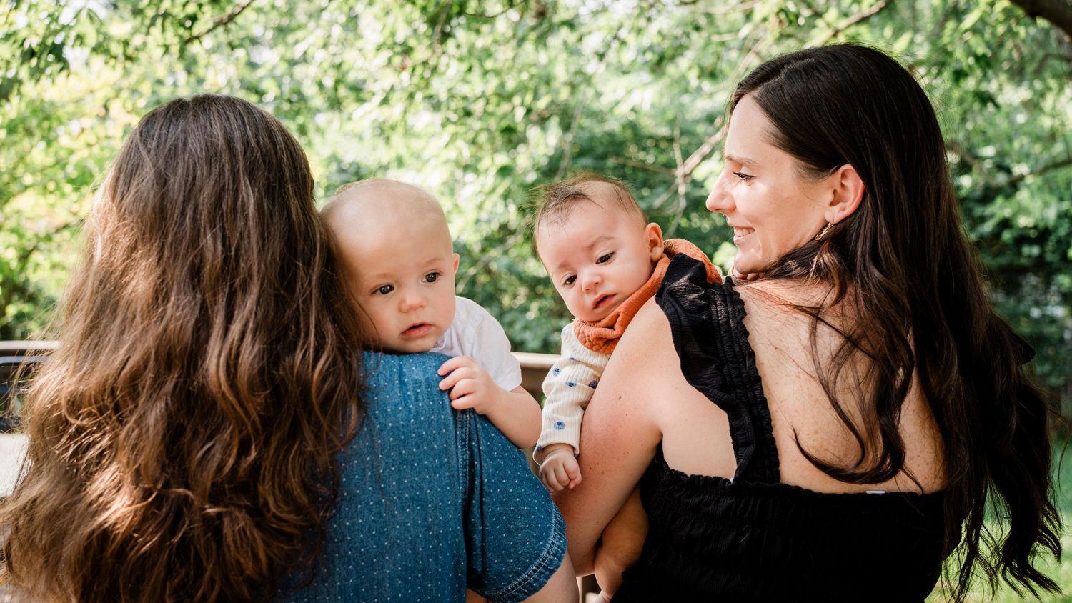 Best friends and their new baby portrait series taken outdoors with lush green foliage background.