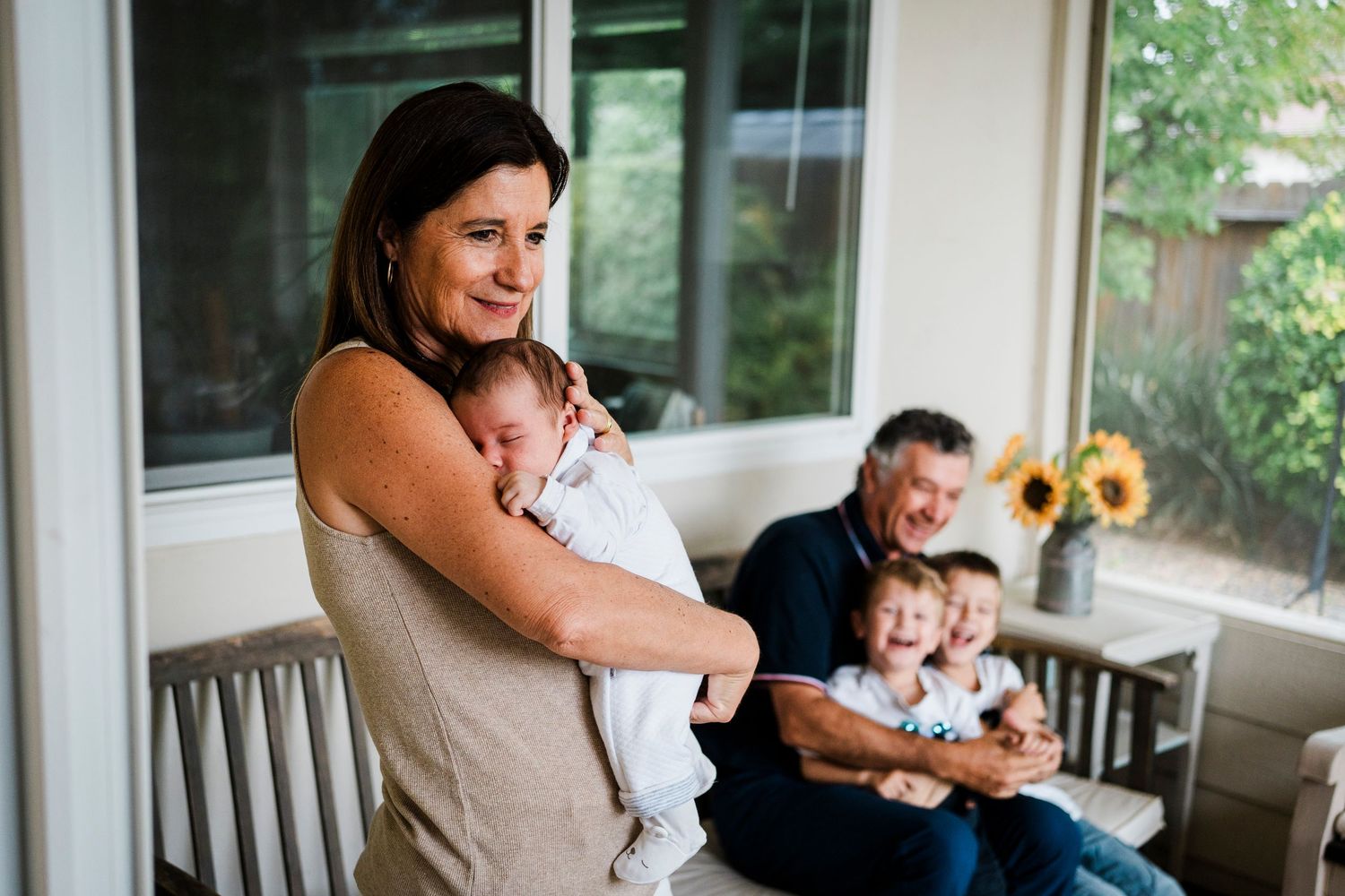 A family shares a tender moment together on an outdoor porch with sunflowers visible in background.