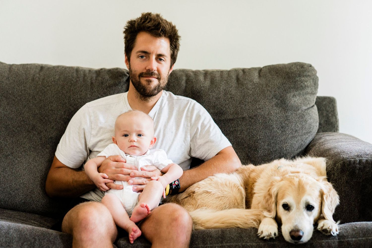 Family relaxing on grey couch with golden retriever dog lounging beside them.