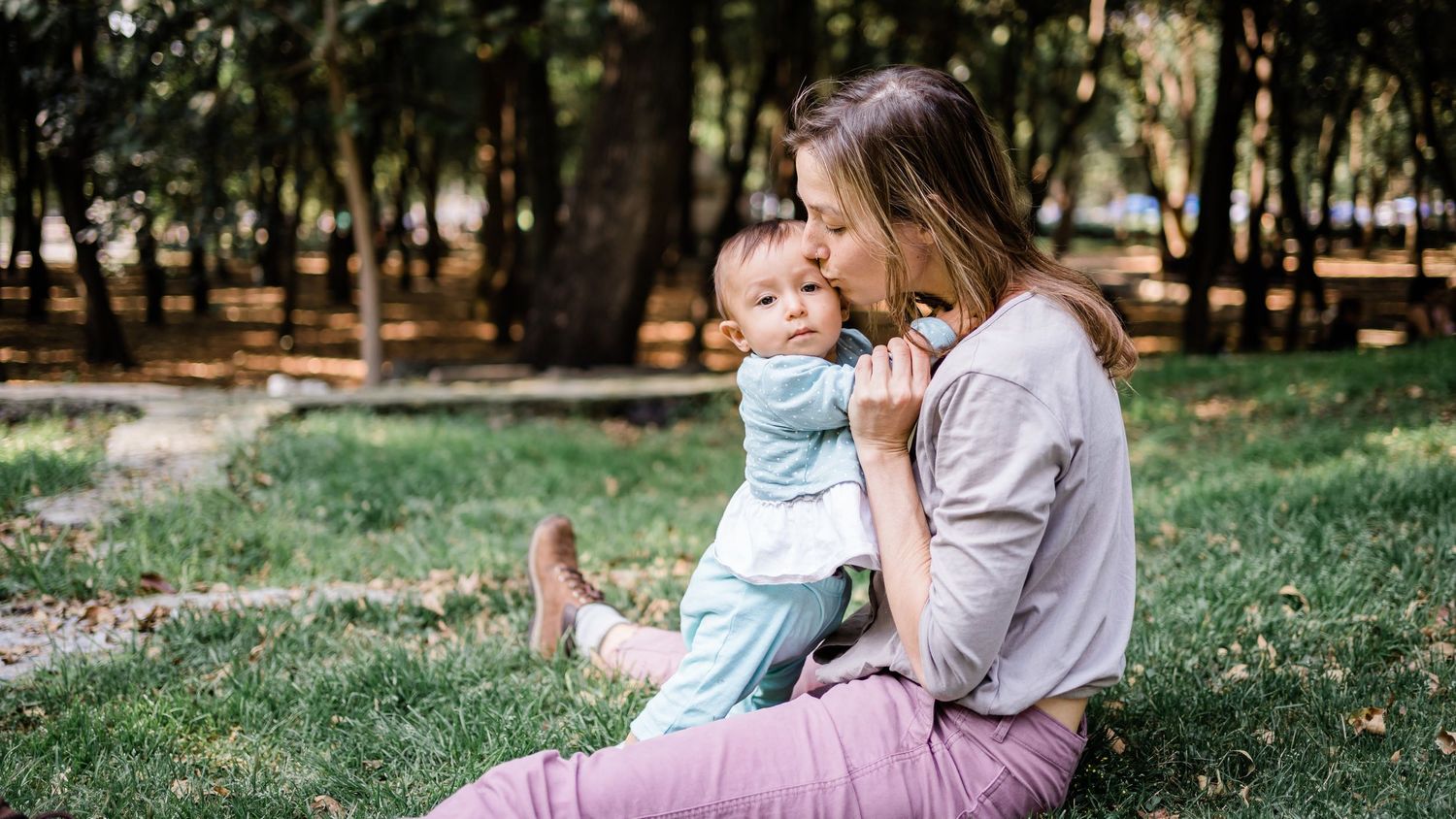 Tender moment shared between two figures sitting together on grass in a park setting.