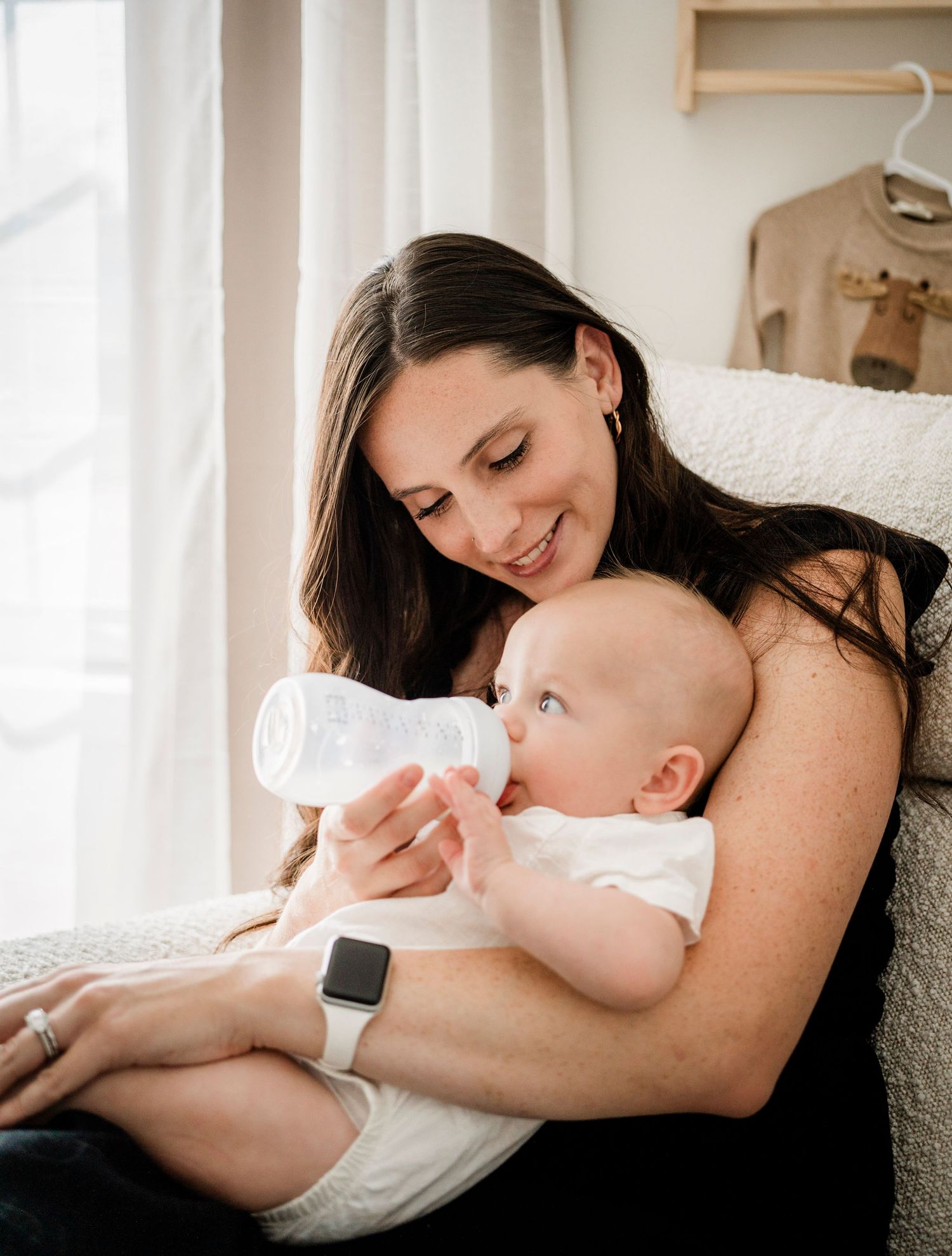 Tender moment of parent and infant bonding while feeding the baby in a serene white room.