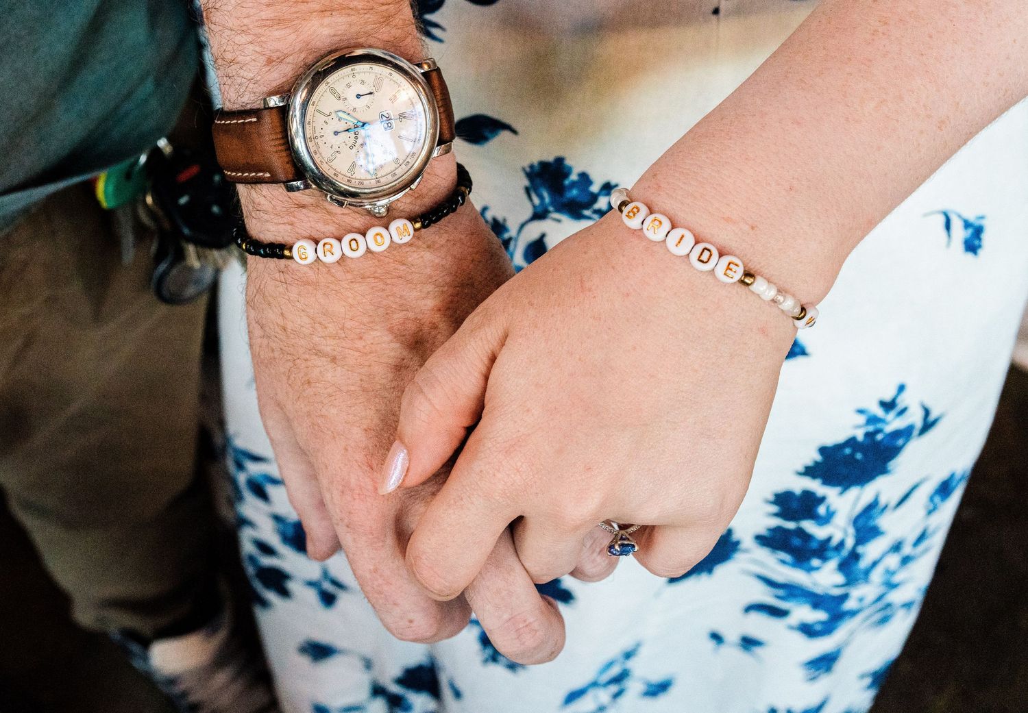 Close-up of hands wearing matching bracelets and a brown leather watch.