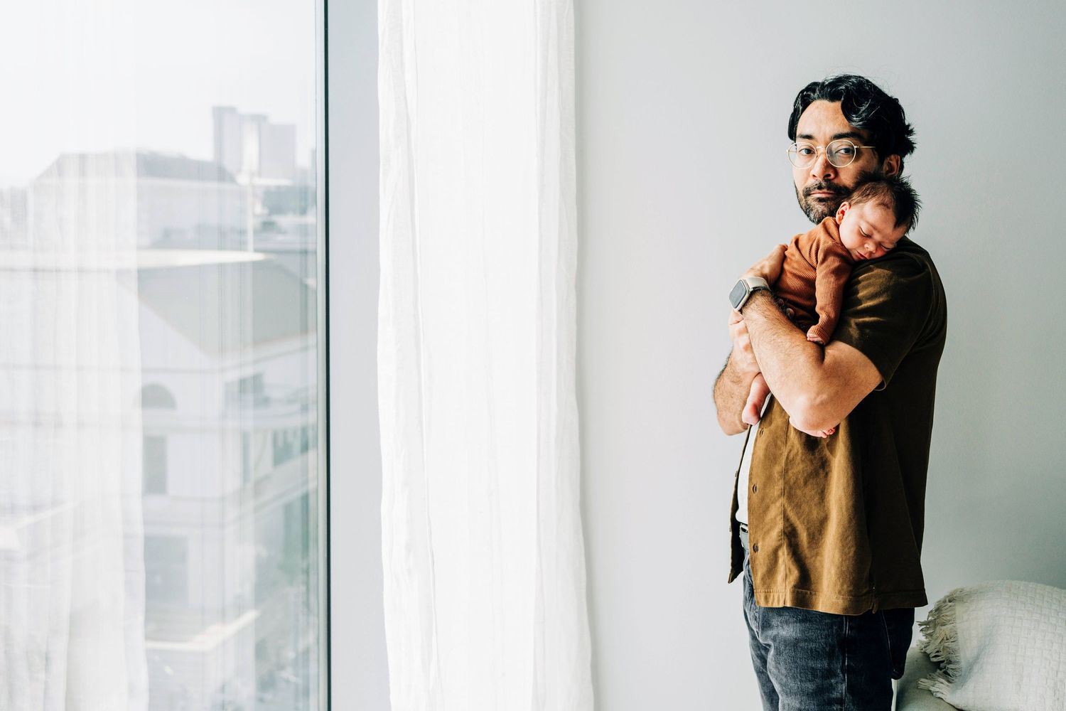 Tender family moments photographed near a bright window in a minimalist setting.