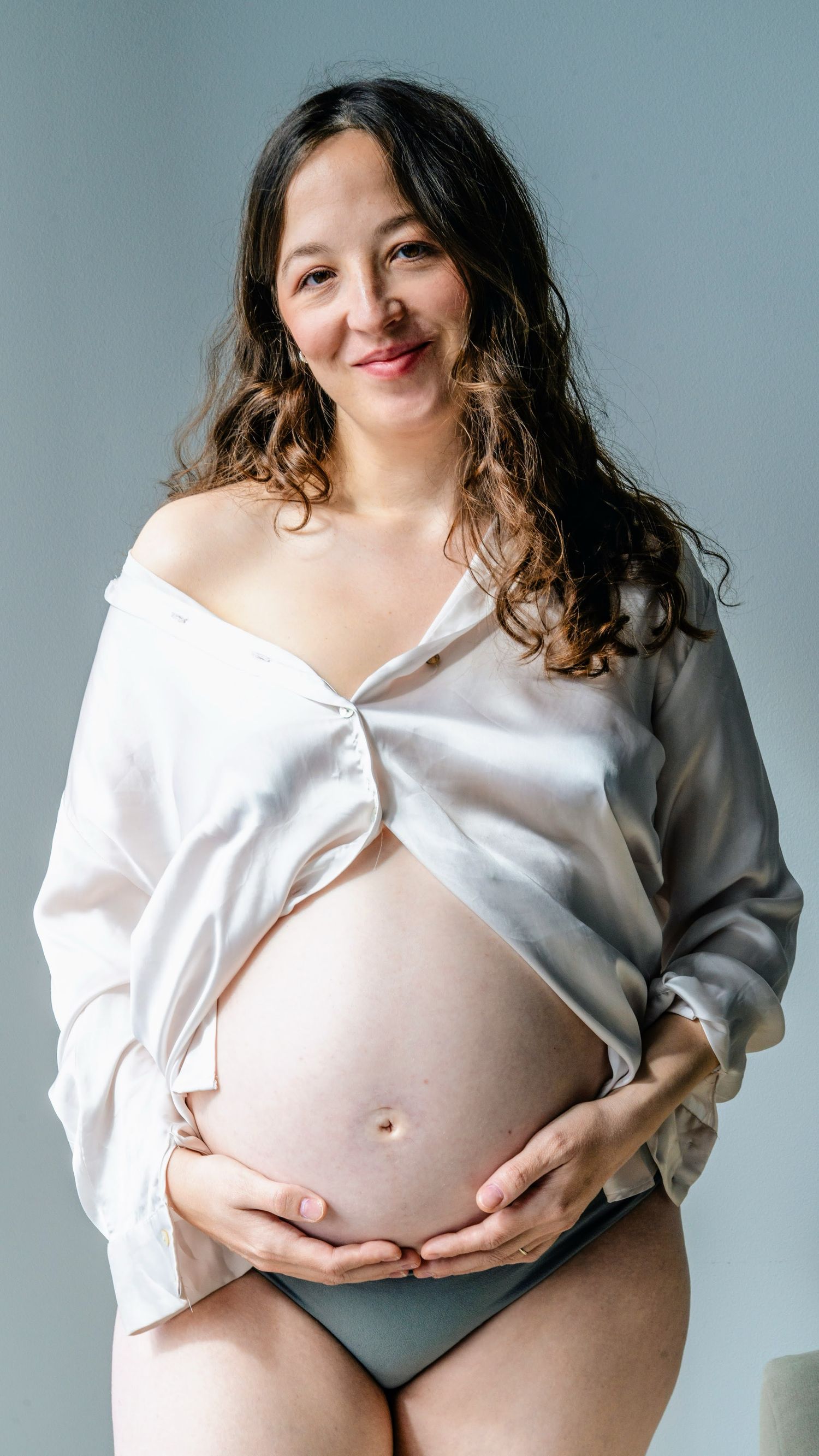 Maternity portrait in white shirt showing pregnancy belly against blue background.