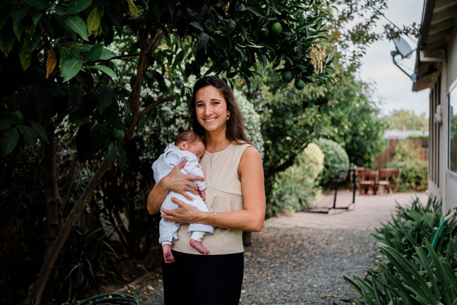 A parent holds a small infant while standing in a garden path surrounded by lush greenery.