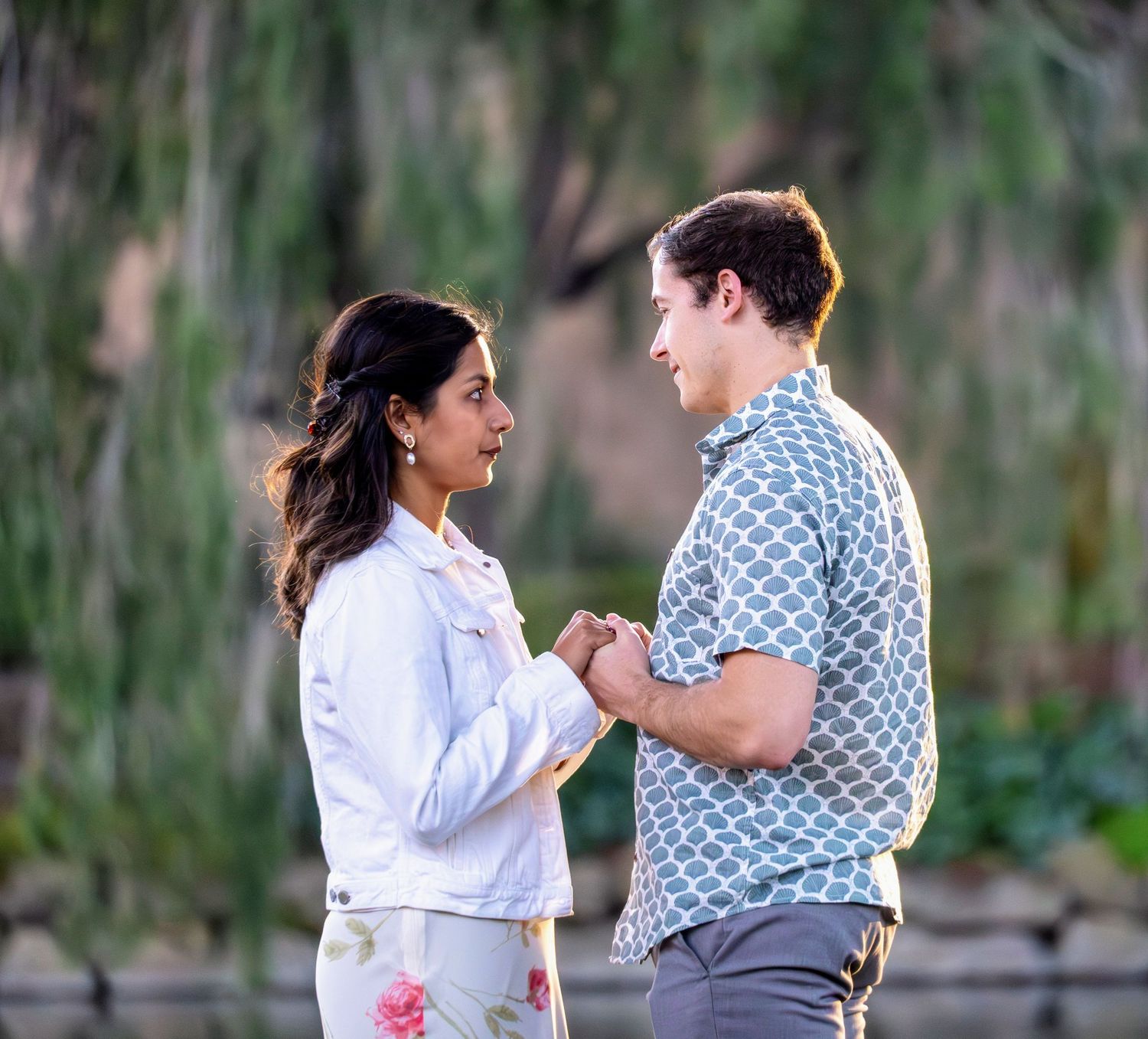 Couple wearing casual outfits embracing outdoors near mossy trees.