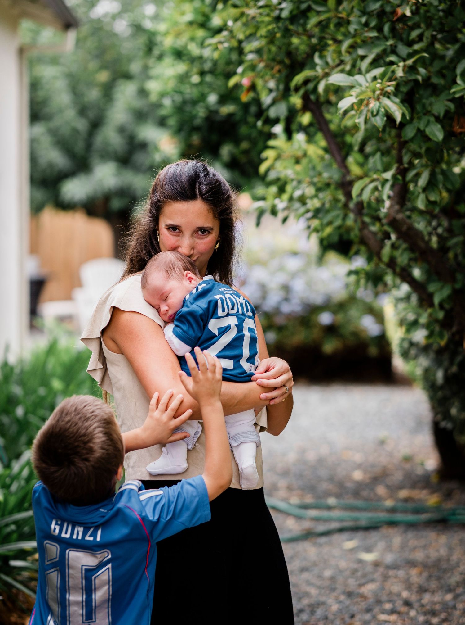 A family plays together outdoors among green foliage and trees in a backyard setting.