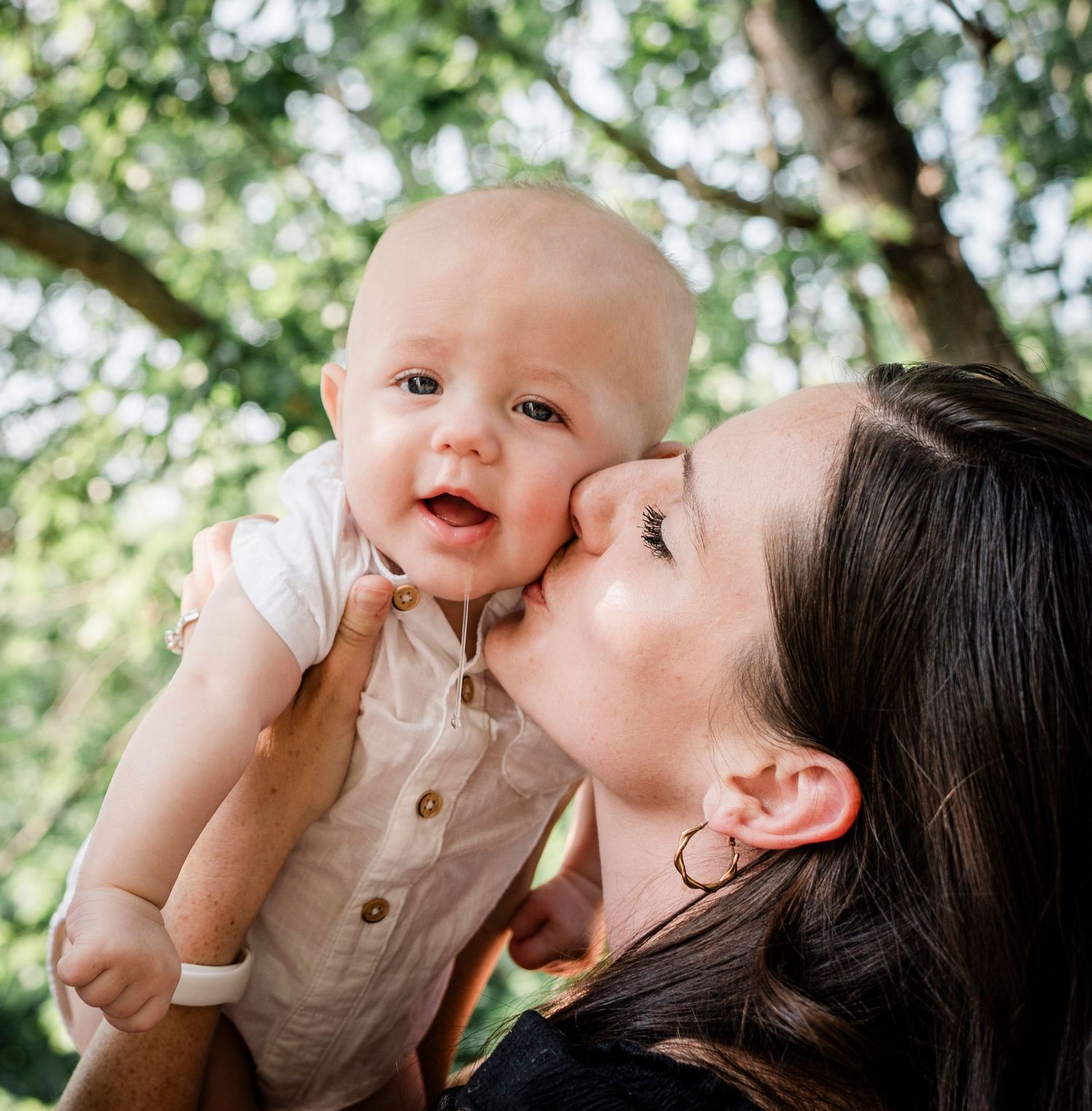 Sweet bonding moments of mother and baby captured outdoors in a garden setting with natural sunlight filtering through trees.