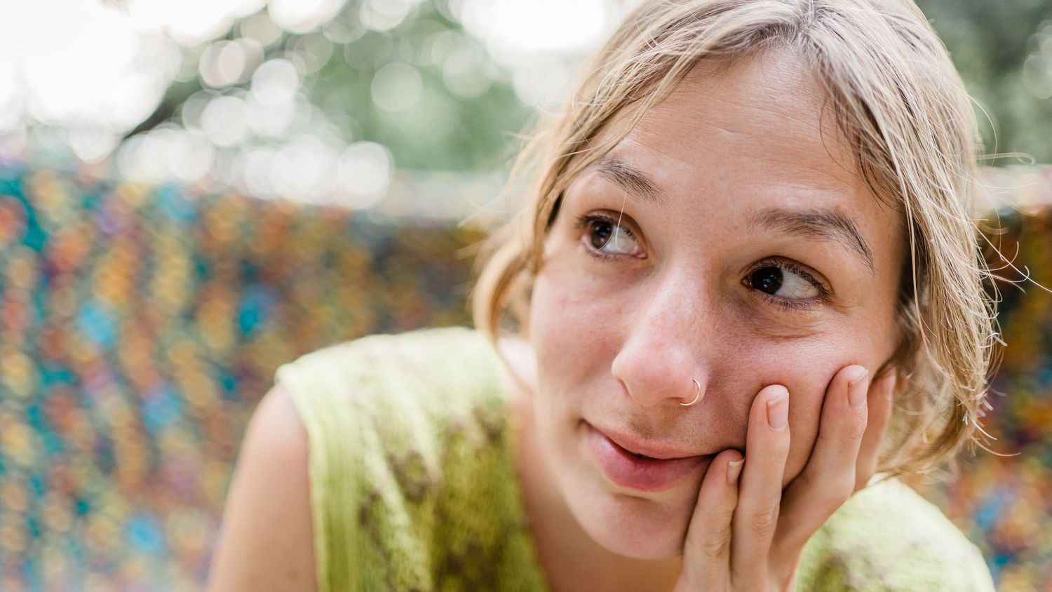 Person in yellow top rests head on hand while relaxing outdoors.