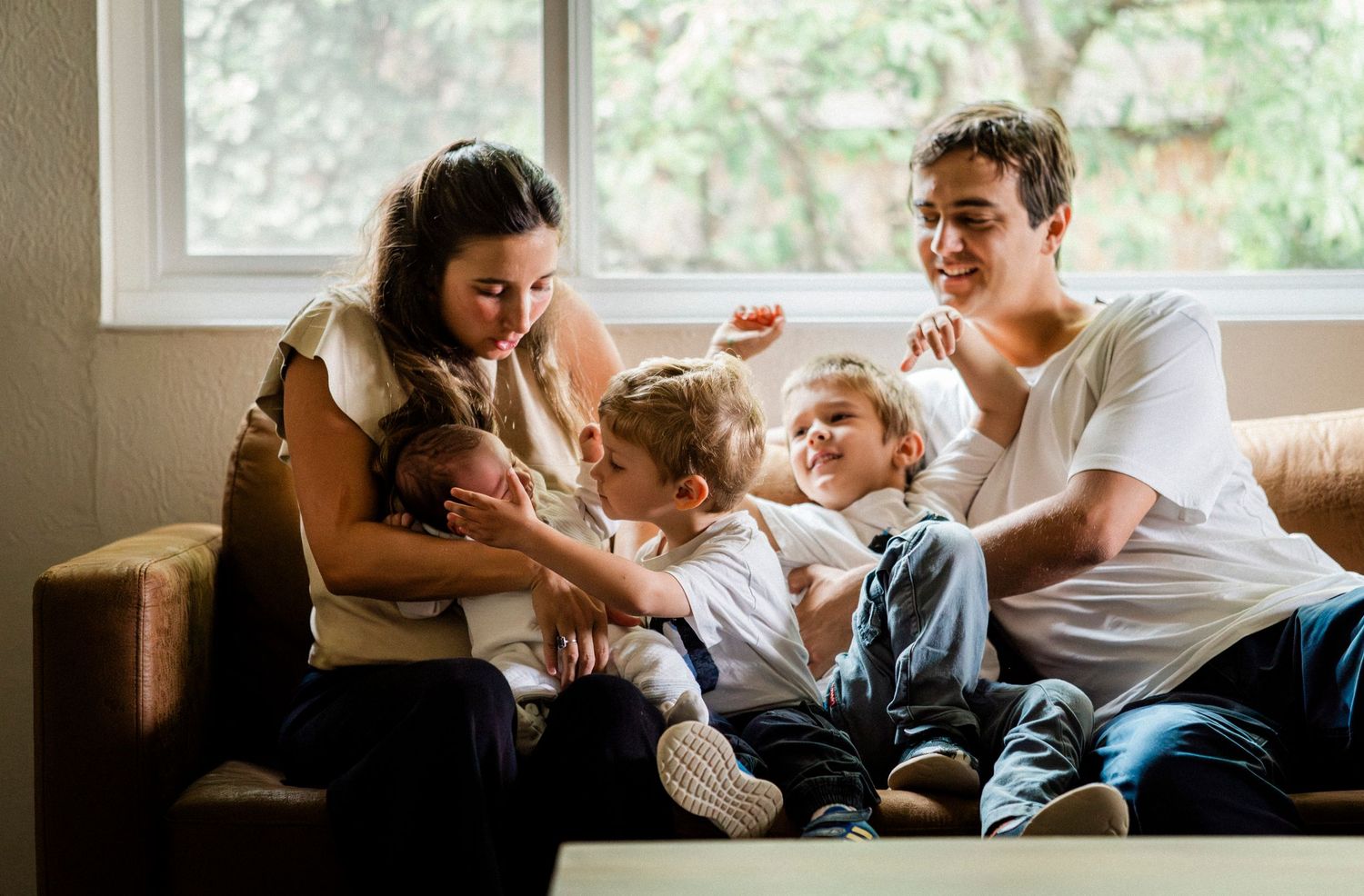 Family relaxing together on couch at home sharing joyful moment in natural window light.